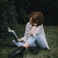 lady reading book while sitting on grassy lawn near plants
