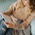 woman in knitted sweater and denim jeans reading a book