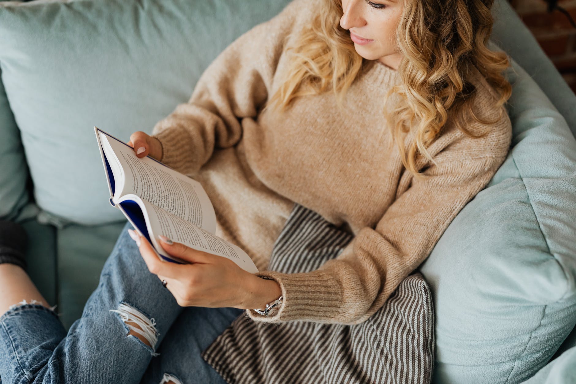 woman in knitted sweater and denim jeans reading a book