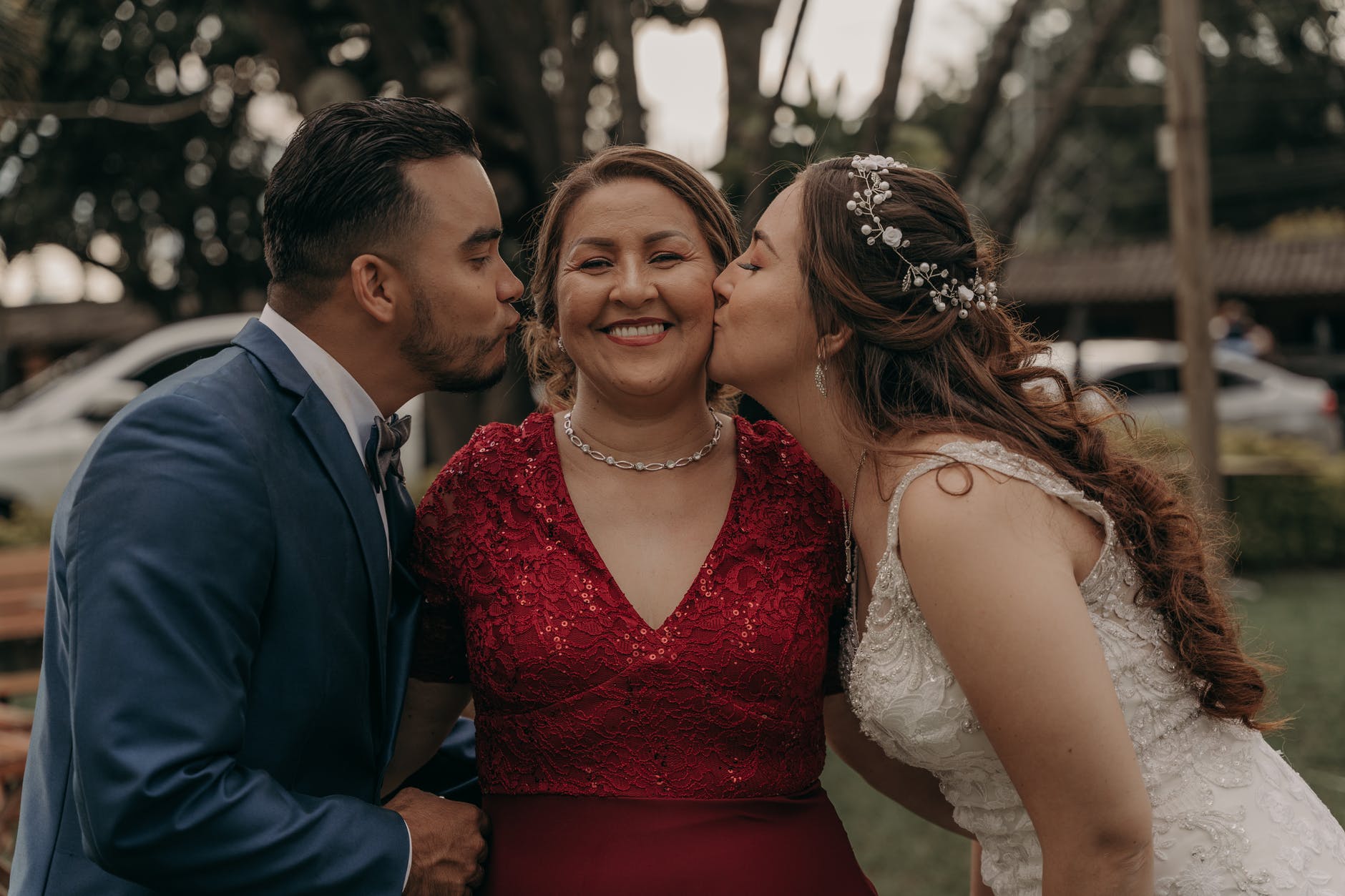 ethnic newlywed couple kissing cheerful mother on wedding day